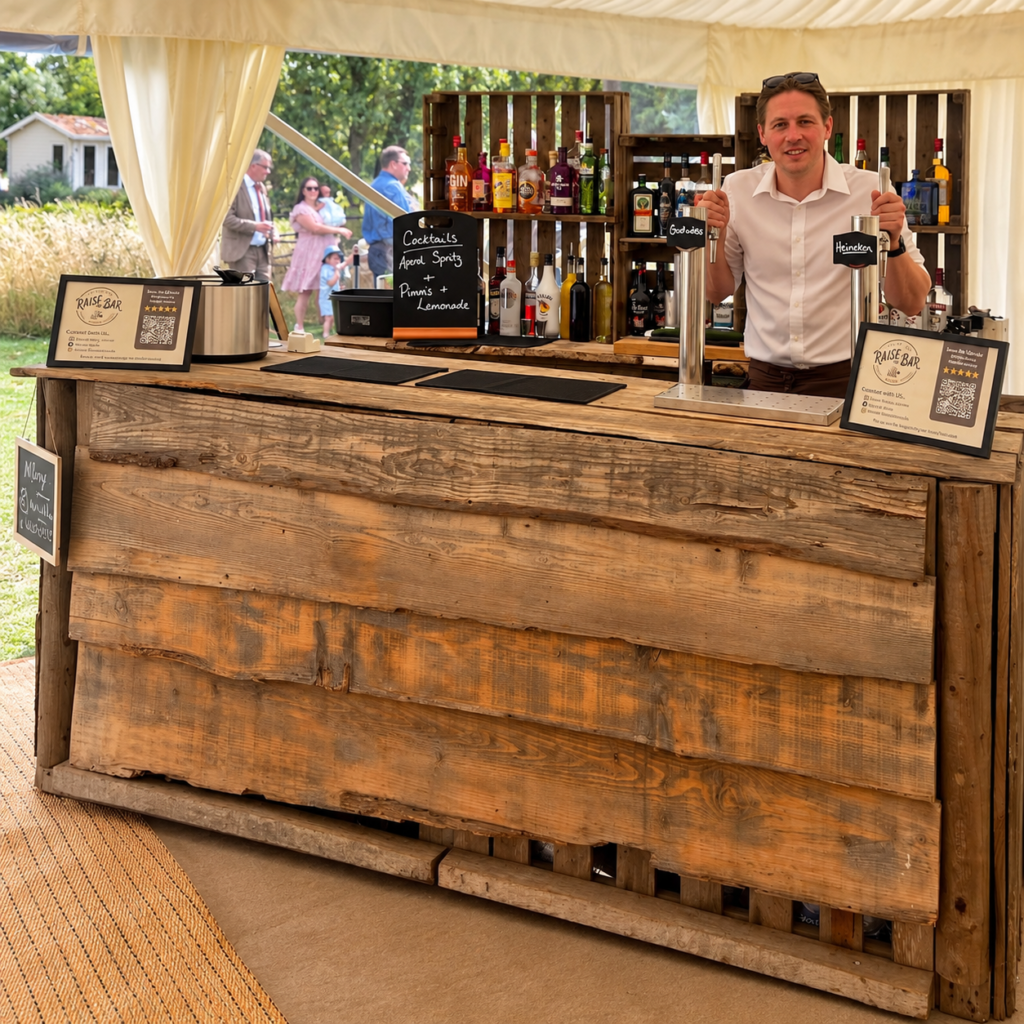 Sammy behind the Raise the Bar rustic wooden mobile bar at a marquee event