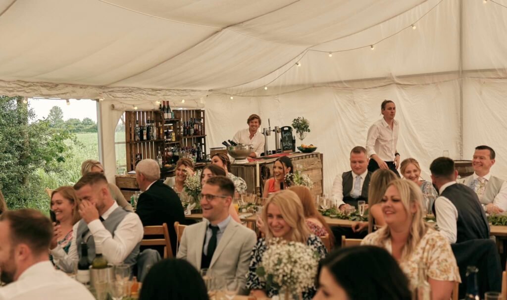 Wedding guests seated in a marquee with the Raise the Bar team behind the bar